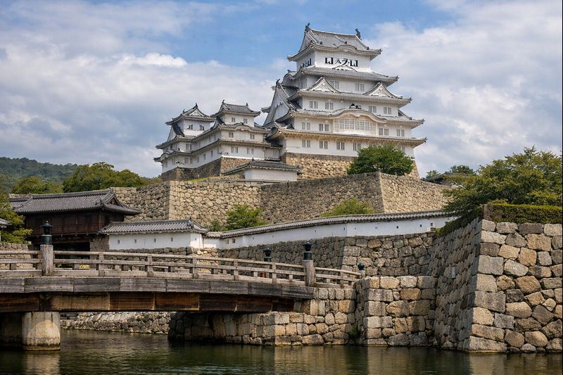 لقطة واقعية لقلعة هيميجي البيضاء على تلة مع أسوار حجرية ومسارات صعود تُوحي بالحصانة والهندسة الدفاعية.